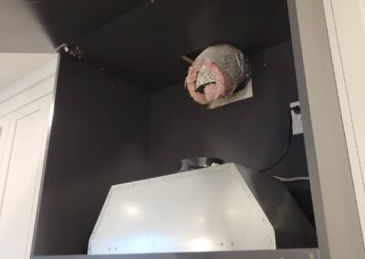 Improperly installed range hood ventilation inside a new home kitchen cabinet, showing exposed ductwork.