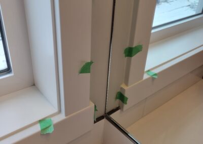 Close-up of a window trim and mirror misalignment in a new home bathroom, marked with green tape.